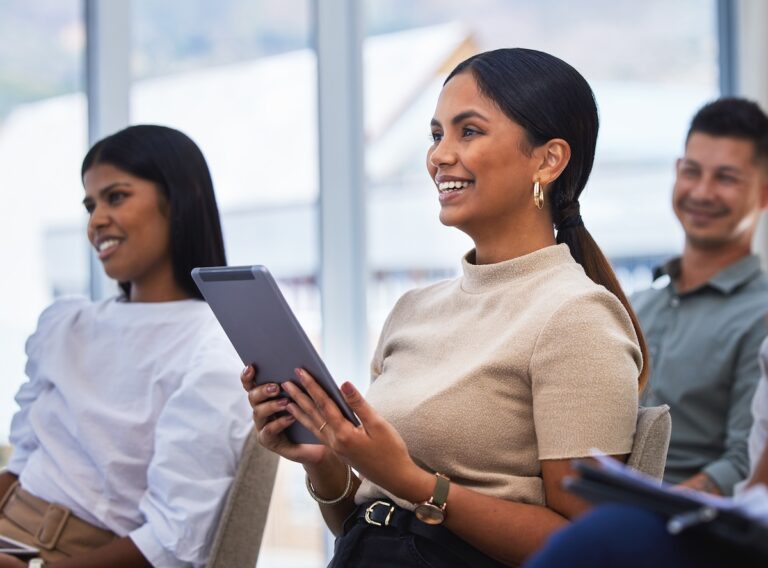 Three people sit at an event with a speak with one woman holding a tablet