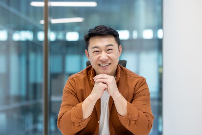 Businessman smiling and looking at the camera with his chip resting on the top of his hands and elbows on the table
