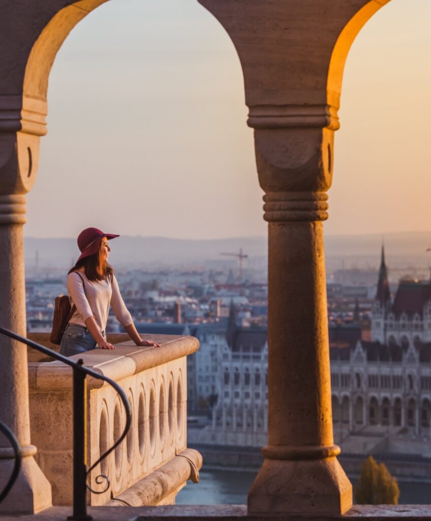 A happy young woman in hat enjoying her trip to the Castle of Budapest in Hungary on the view point from Fisherman Bastion on sunrise.